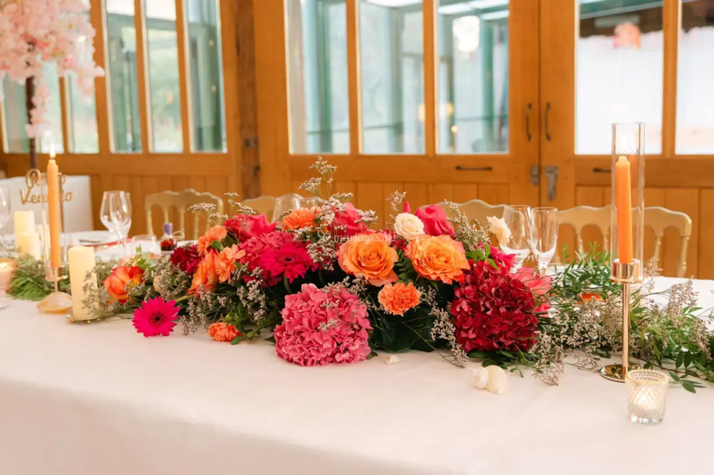 Arrangement floral coloré sur une table dressée, avec des bougies et des verres, dans un cadre élégant.