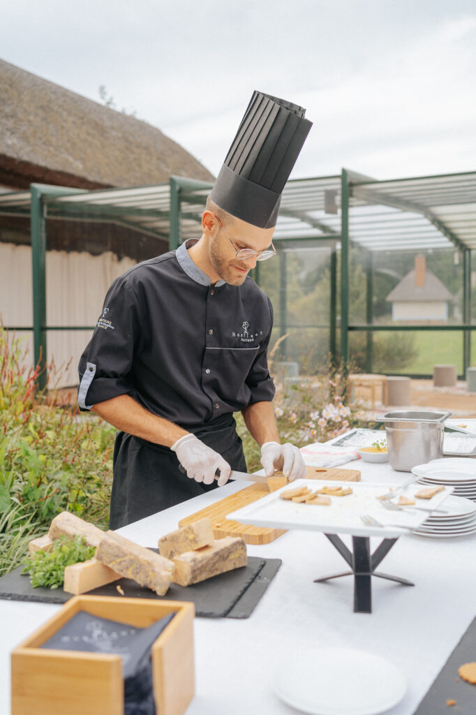 Chef aux gestes précis, préparant des plats en extérieur, avec des ingrédients frais sur une table dressée à Tourgéville.