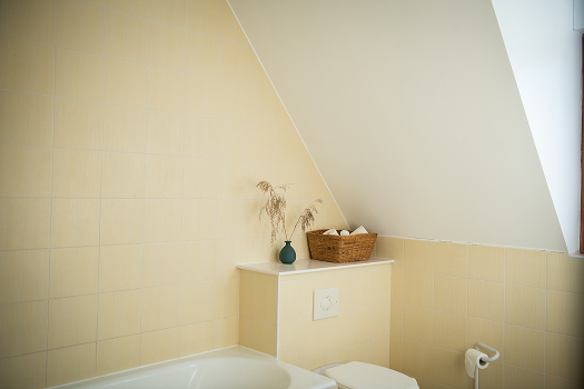 Salle de bains lumineuse avec murs jaunes, baignoire, éléments de décoration et rangement.
