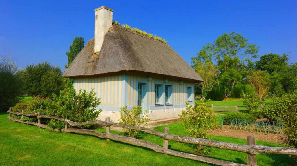 Chaumière normande avec toit de chaume, entourée de jardins verdoyants et de haies, située à Tourgéville en Normandie.