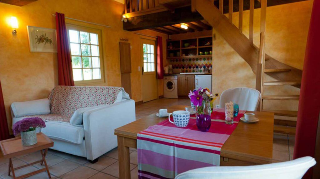 Intérieur chaleureux du gîte Chaumière Les Noyers, avec salon accueillant, kitchenette et décoration colorée.