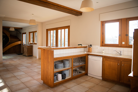 Cuisine spacieuse et lumineuse du gîte, avec comptoir en bois, vaisselle et vue sur l'extérieur. Parfait pour un séjour en Normandie.