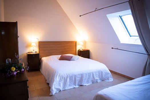 Chambre cosy avec lits doubles, lampe de chevet, et fenêtre sous les combles, parfaite pour un séjour à la Maison de la Mare.