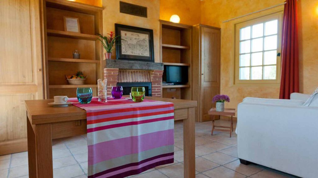Intérieur chaleureux de la Chaumière Les Peupliers avec une table décorée, cheminée et lumière naturelle. Idéal pour des séjours en Normandie.