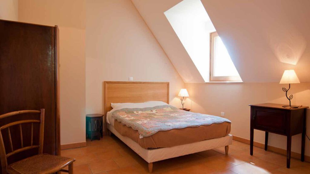 Chambre de gîte avec lit double, lampes de chevet et fenêtre sous le toit, décorée avec une couverture colorée.