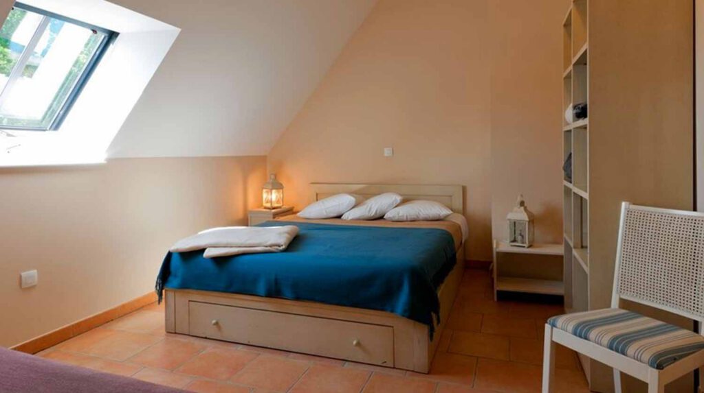 Chambre cosy au gîte, avec lit confortable, éclairage doux et mobilier pratique, idéale pour un séjour relaxant en Normandie.