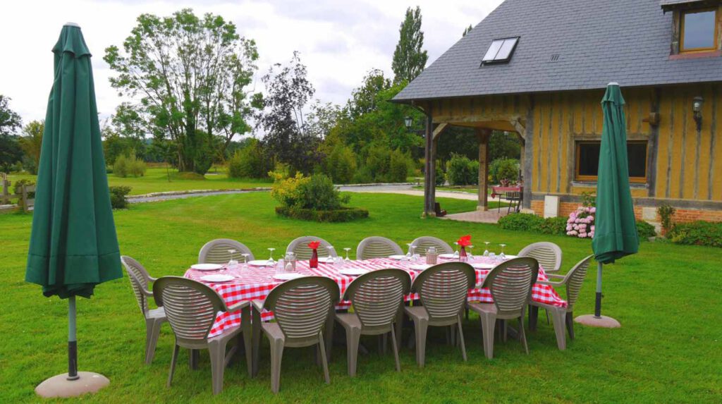 Table dressée avec nappes à carreaux rouges et chaises sur la pelouse, au pied d'une maison normande. Ambiance chaleureuse pour événements.