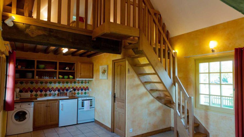 Intérieur lumineux d'un gîte avec cuisine équipée et escalier en bois, décoré dans des tons chauds.