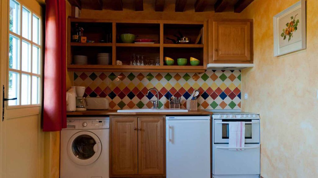 Cuisine chaleureuse avec éléments en bois, carrelage coloré, lave-linge et espace pour repas à la Chaumière Les Noyers en Normandie.