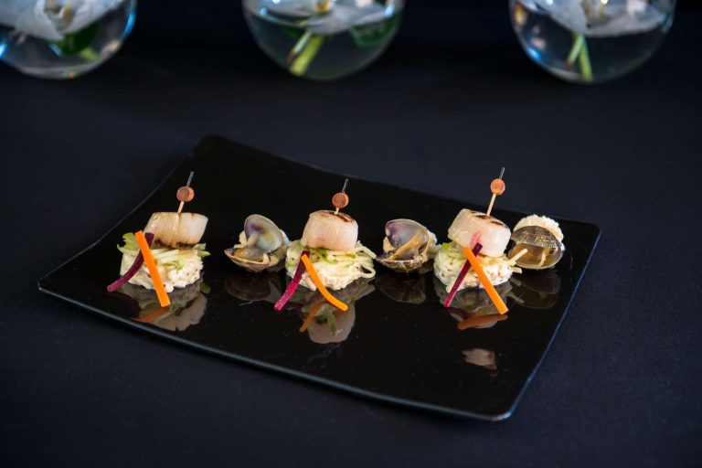 Mise en scène de hors-d'œuvre raffinés sur assiette noire, avec des ingrédients colorés et des garnitures élégantes.