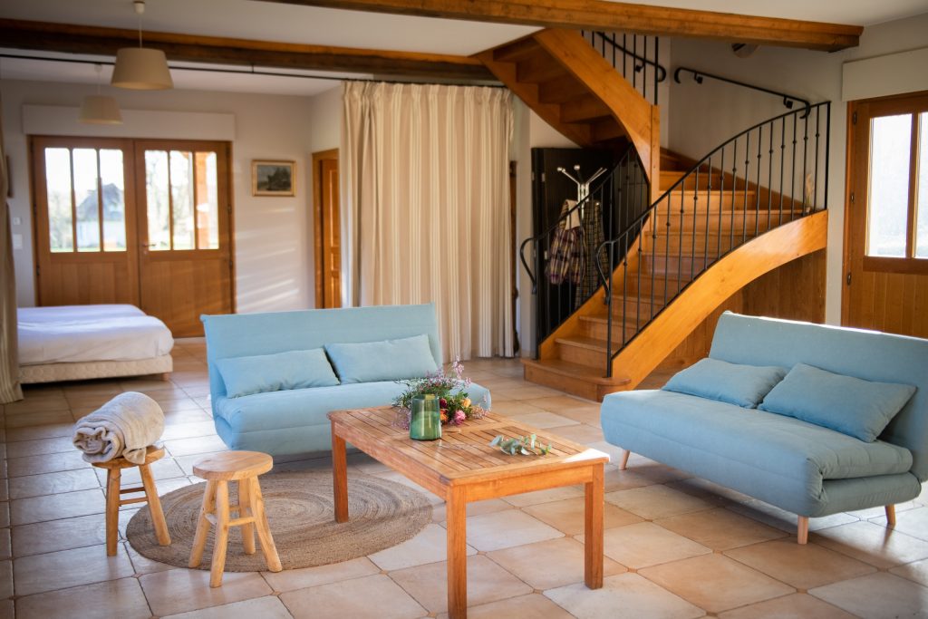 Intérieur accueillant du Pressoir de Tourgéville avec canapés bleus, table en bois, et escaliers en bois.