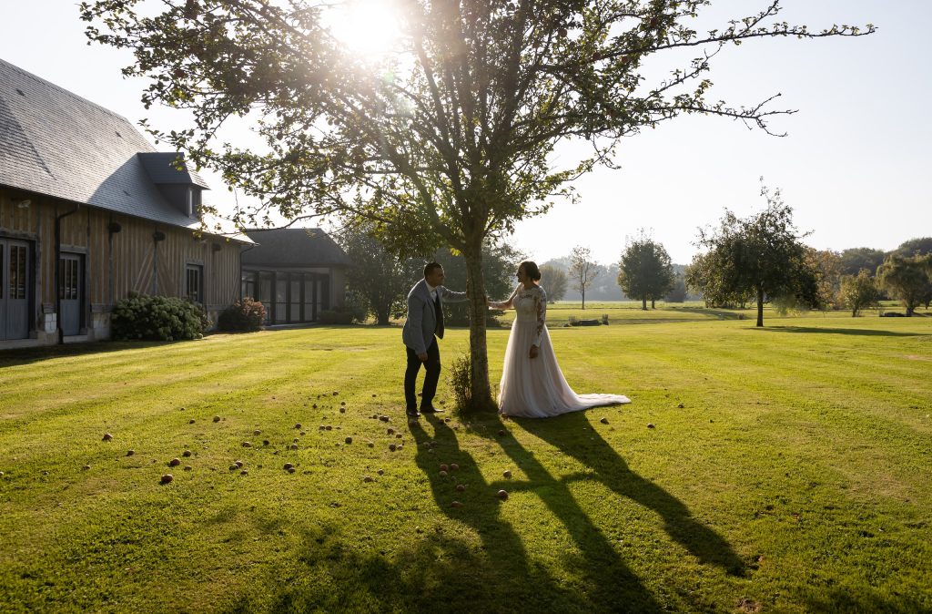 Couple en mariage sous un arbre dans un jardin en Normandie, avec lumière douce et cadre champêtre.
