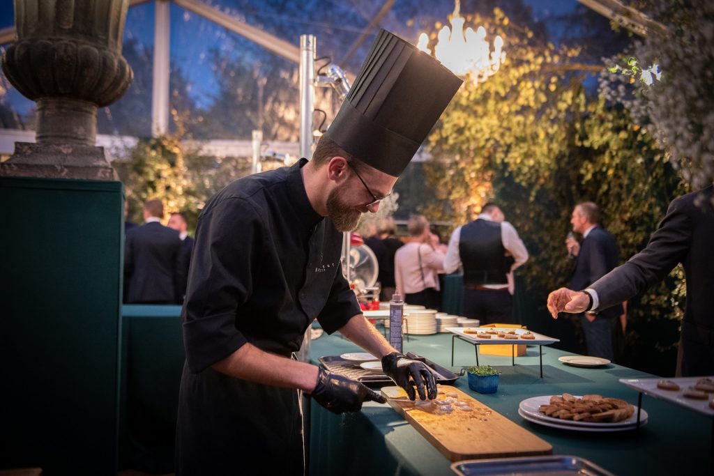 Chef en train de préparer des plats raffinés lors d'un événement privé en Normandie, avec des convives en arrière-plan.