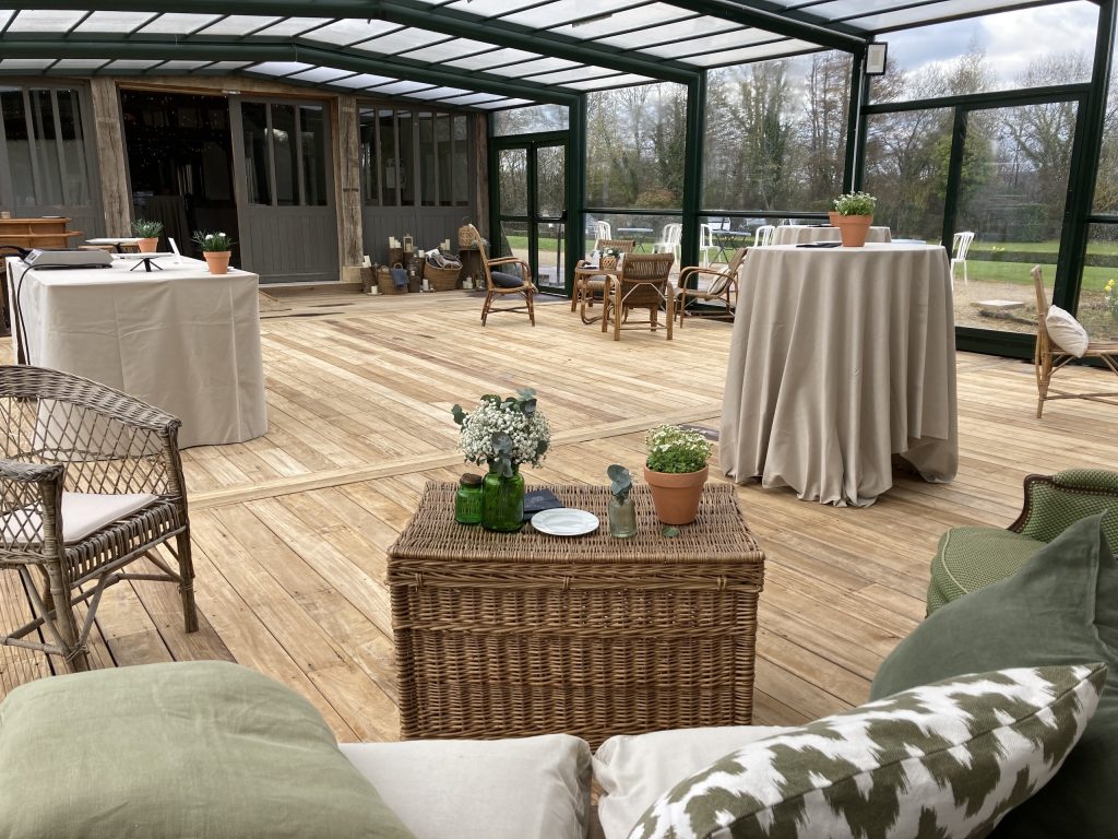 Espace intérieur lumineux pour événements, avec tables, chaises, décoration élégante et vue sur le jardin en Normandie.